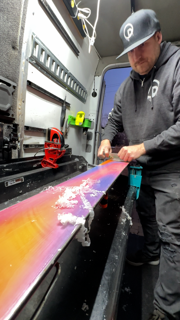 Professional technician hand-tuning colorful skis in mobile workshop demonstrating expert craftsmanship